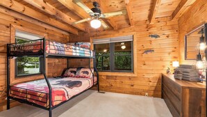 Een slaapkamer met stapelbed, plafondventilator, twee ramen en een dressoir met handdoeken.