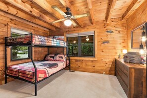 Une chambre avec un lit superposé, un ventilateur de plafond, deux fenêtres et une commode avec des serviettes.