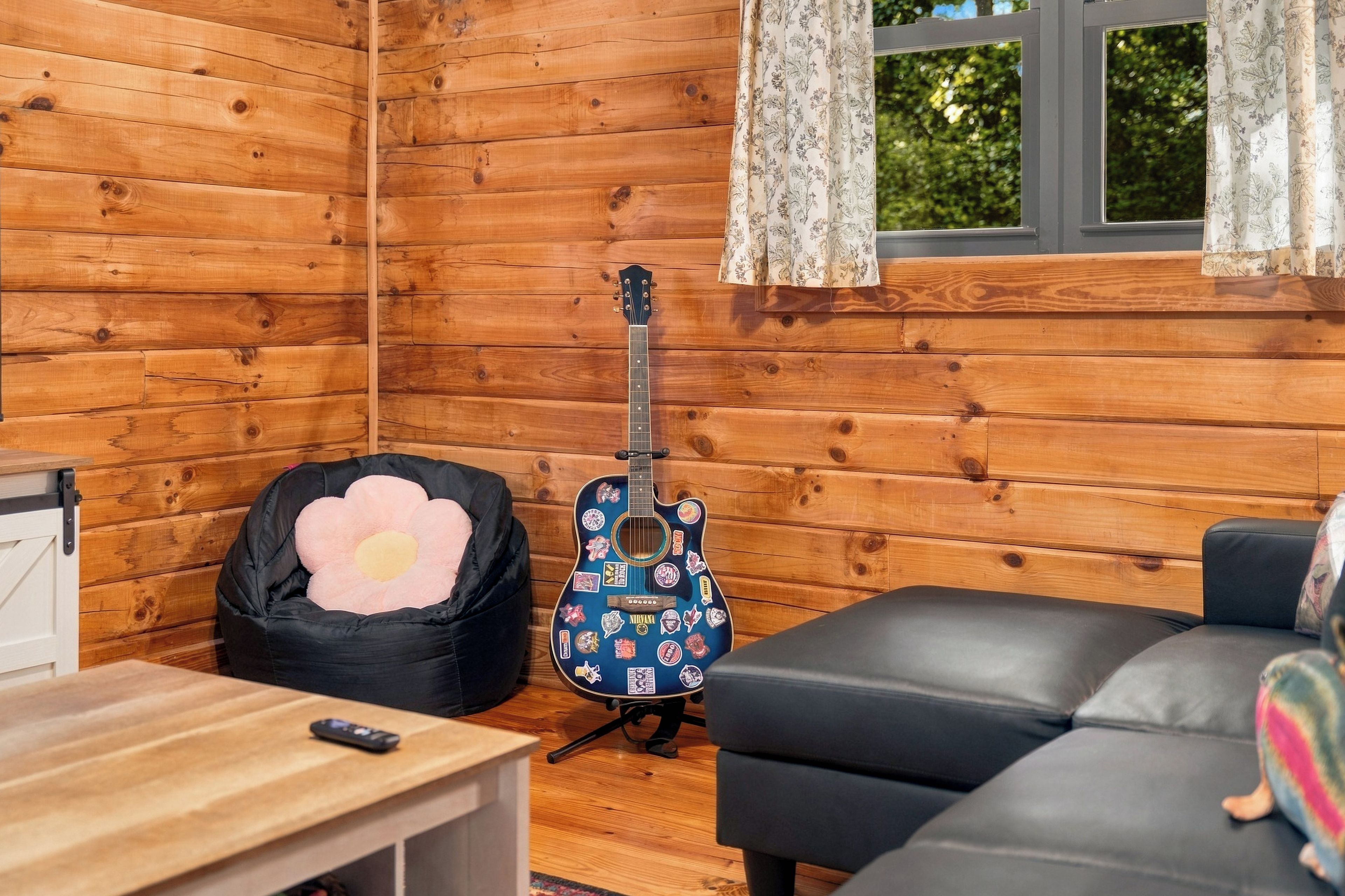 Interior de una cabaña de madera con una guitarra, un sillón informal y un sofá.