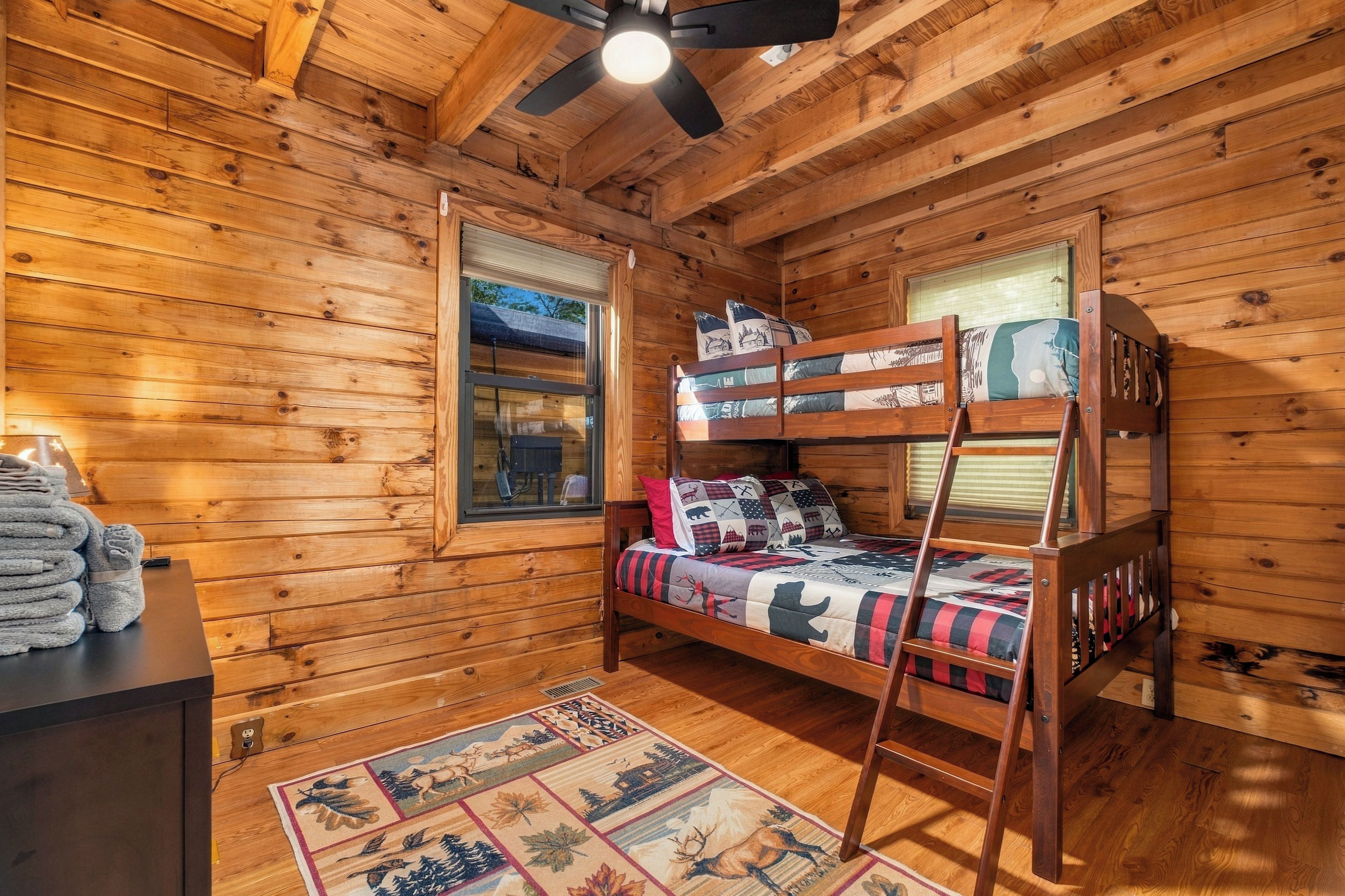 Una habitación tipo cabaña de madera con literas, una ventana, un escritorio con toallas y una alfombra.