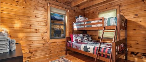 Ein Holzhütten-Zimmer mit Etagenbetten, einem Fenster, einem Schreibtisch mit Handtüchern und einem Teppich.