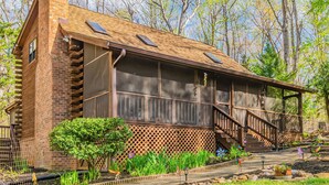 A rustic log cabin with a wooden deck, a staircase, and a fenced garden area.