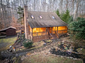 A cabin with a porch, a chimney, and a small shed.