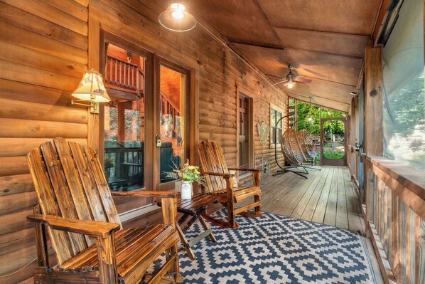 A wooden cabin with a porch, two rocking chairs, a table with a vase, and a patterned rug.