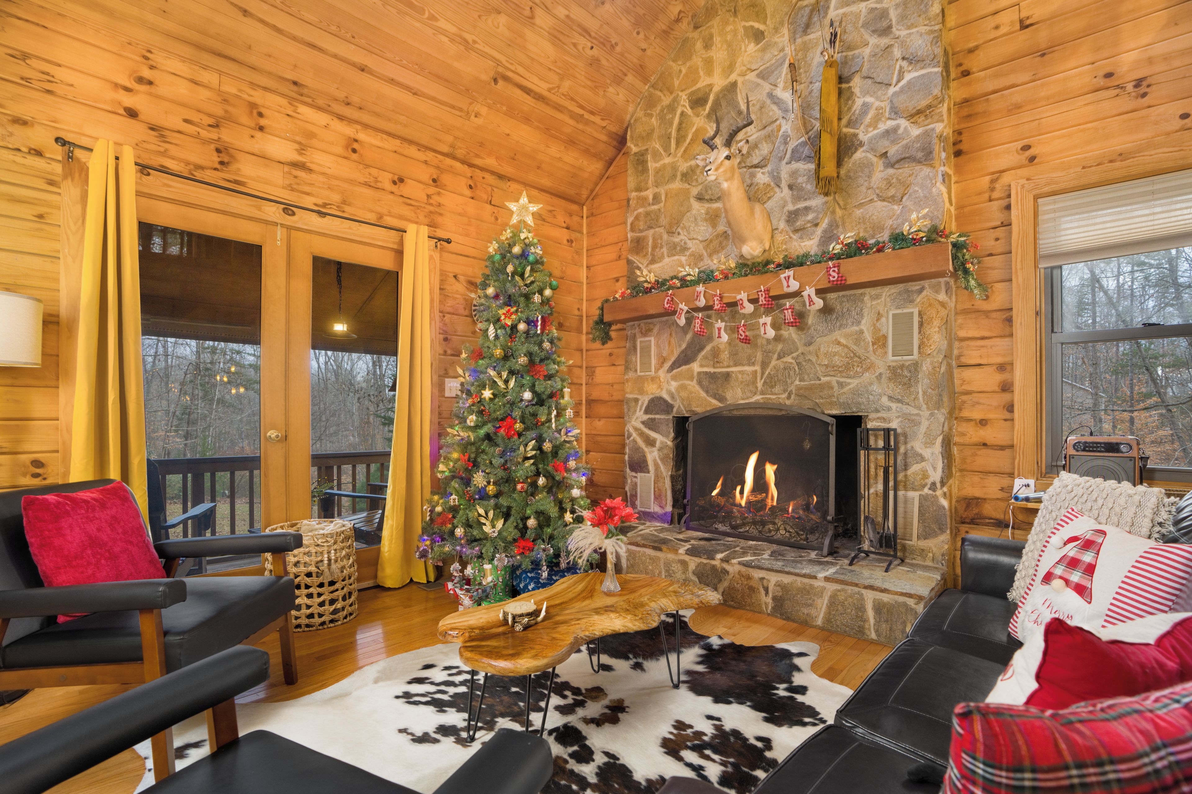 A cozy cabin interior with a stone fireplace, a Christmas tree, and a log wall.