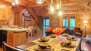 A wooden cabin interior with a dining table set for four, a kitchen area, and a staircase.