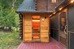 Une cabane en bois avec une porte d’entrée en verre, une terrasse en bois rouge et un mur extérieur noir.