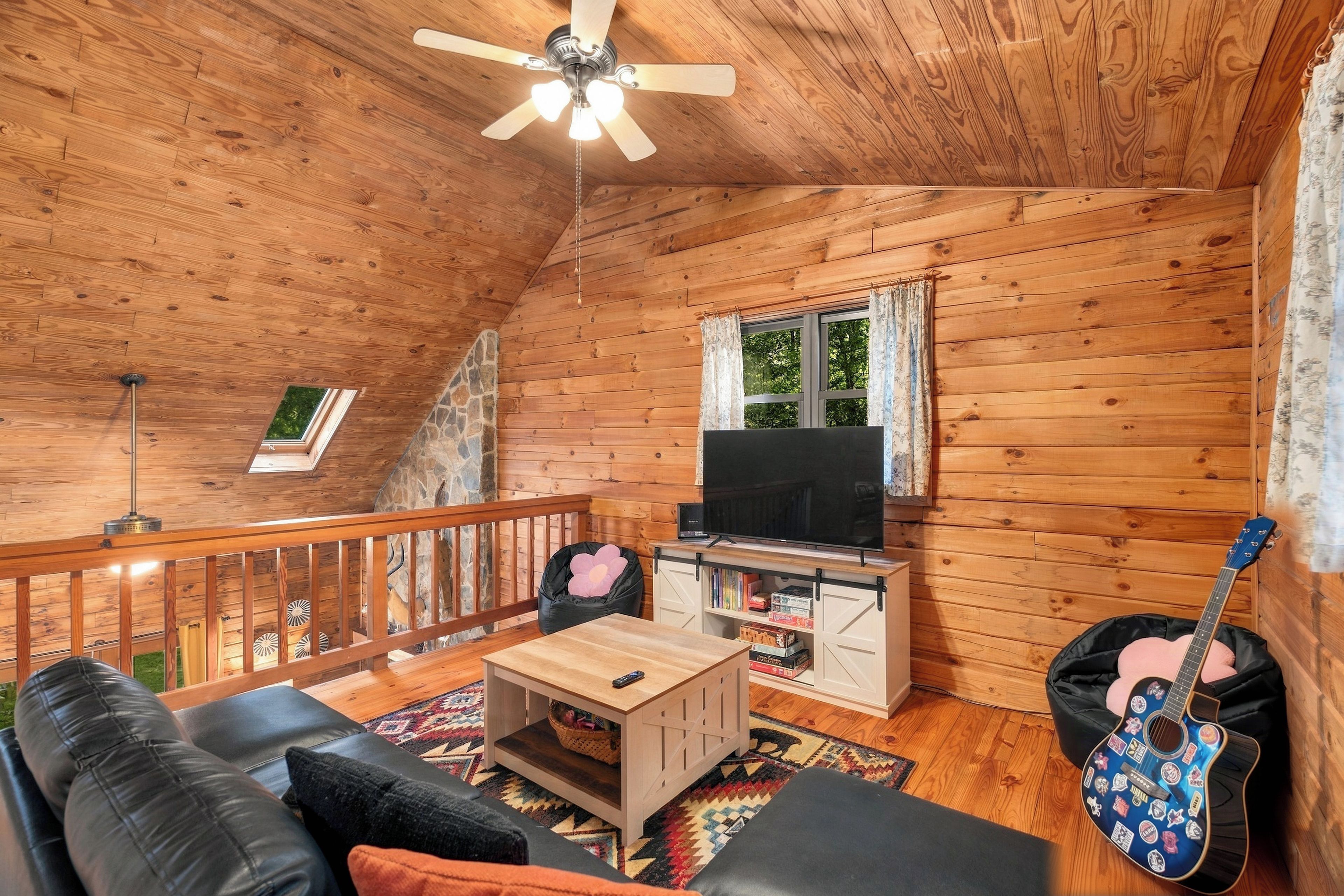 A wooden cabin interior with a ceiling fan, a television, a guitar, and a cozy seating area.