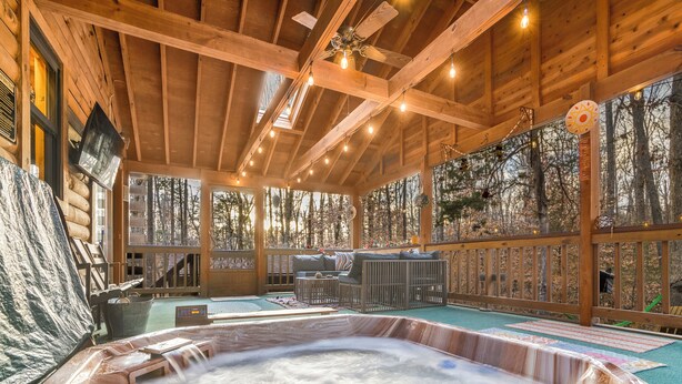A wooden cabin with a hot tub, wooden deck, and a view of the forest.