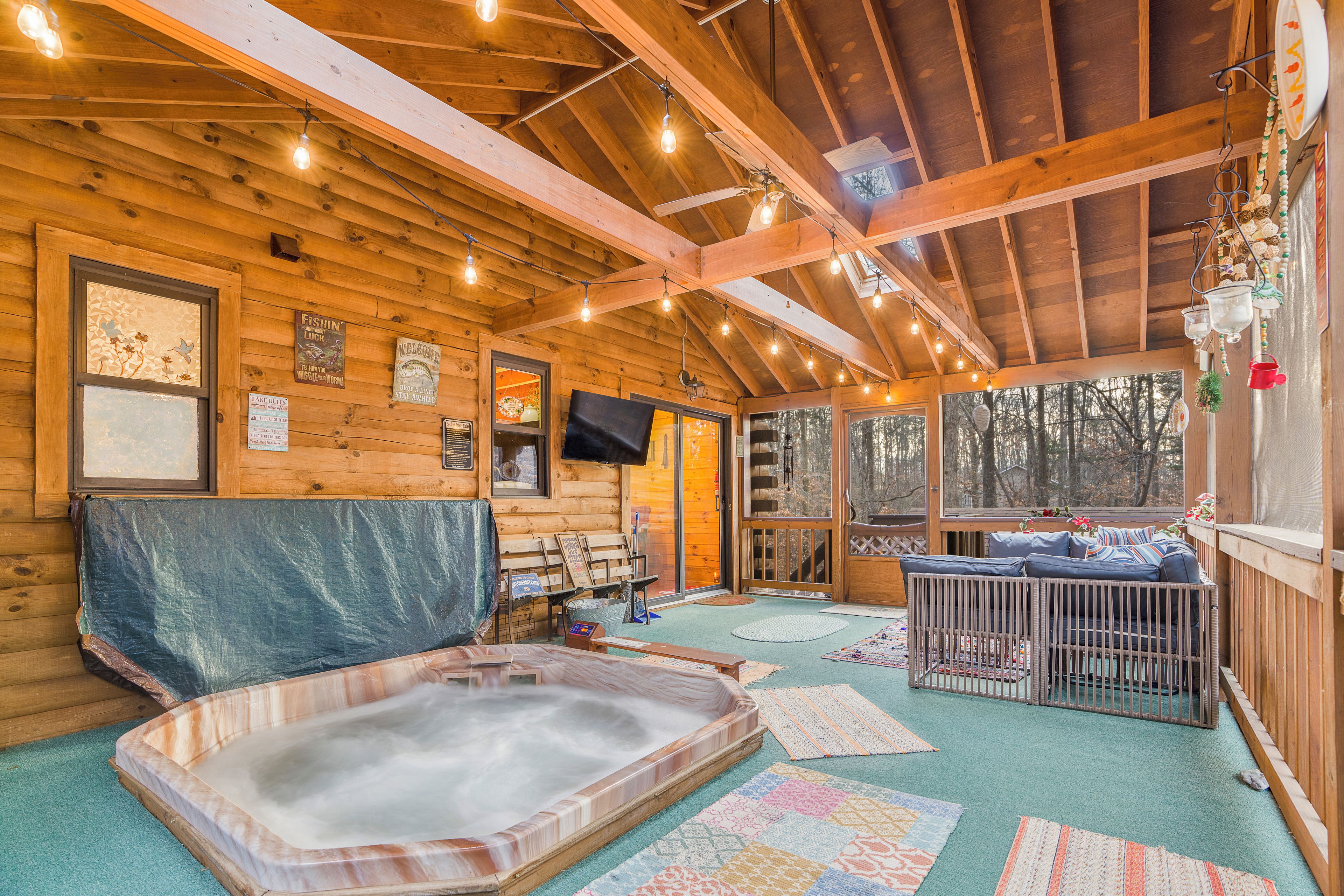 A wooden cabin with a hot tub, seating area, and a large window overlooking trees.
