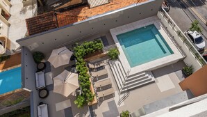 An aerial view of a rooftop pool area with a swimming pool, sun loungers, umbrellas, and potted plants. - Stay Home João Cachoeira - Piscina - Gym (São Paulo)
