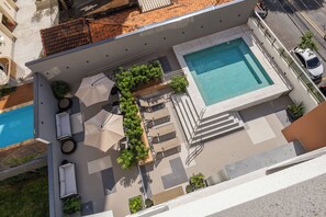 Vista aérea de una zona de piscina en azotea con piscina, tumbonas, sombrillas y plantas en macetas.