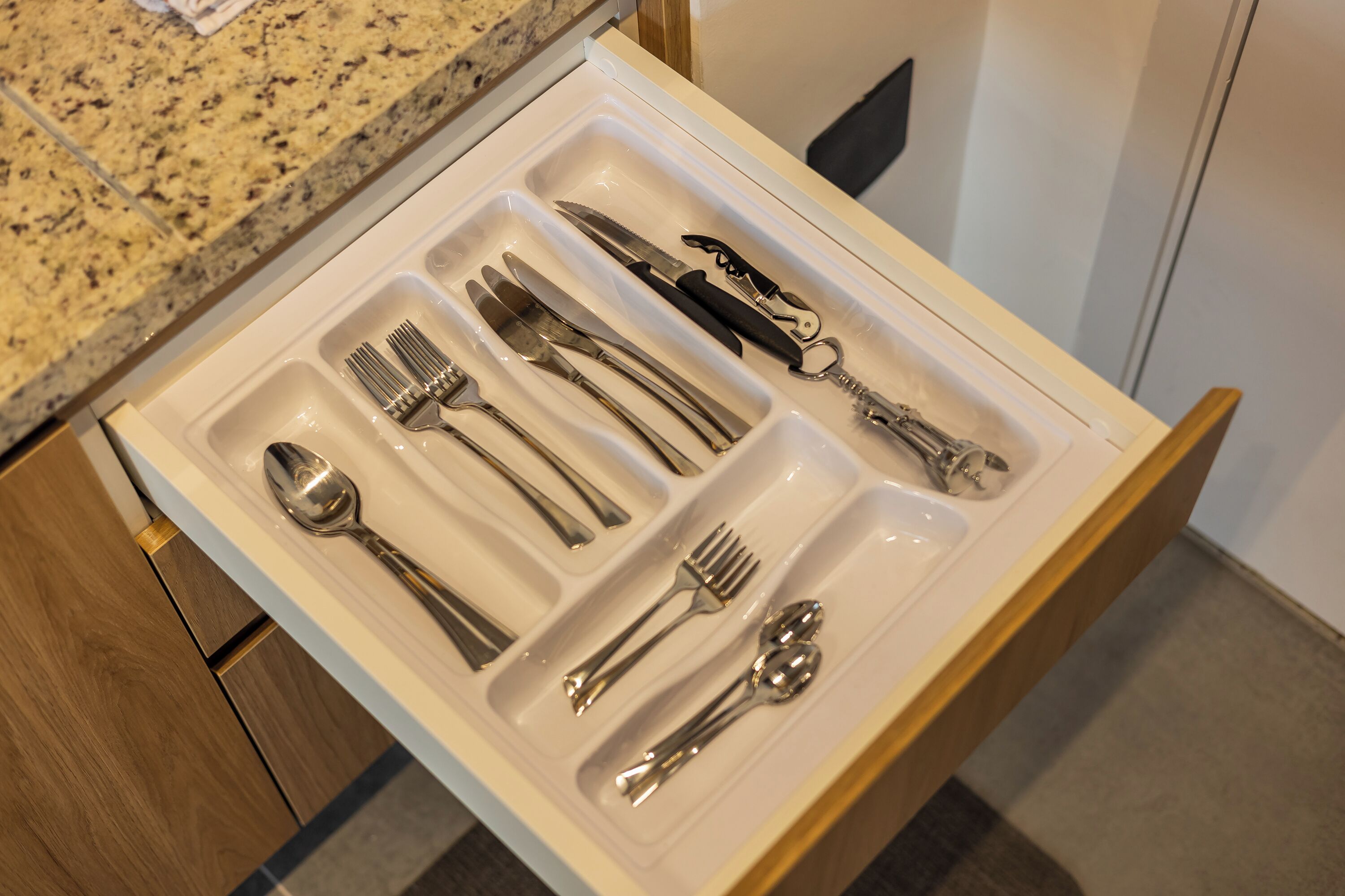 A drawer with neatly arranged cutlery including forks, knives, spoons, and a bottle opener.