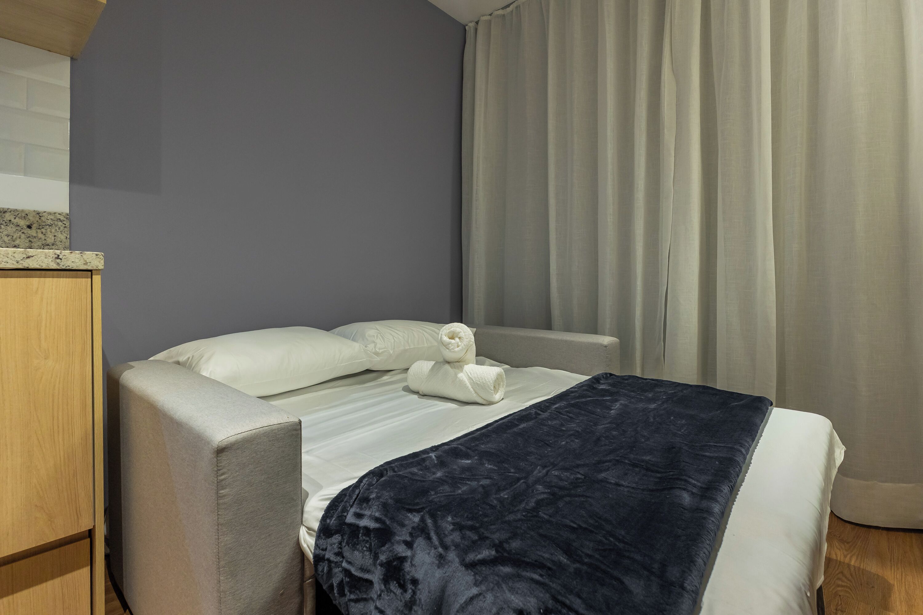 A hotel room with a bed, a wooden wardrobe, and a window with curtains.