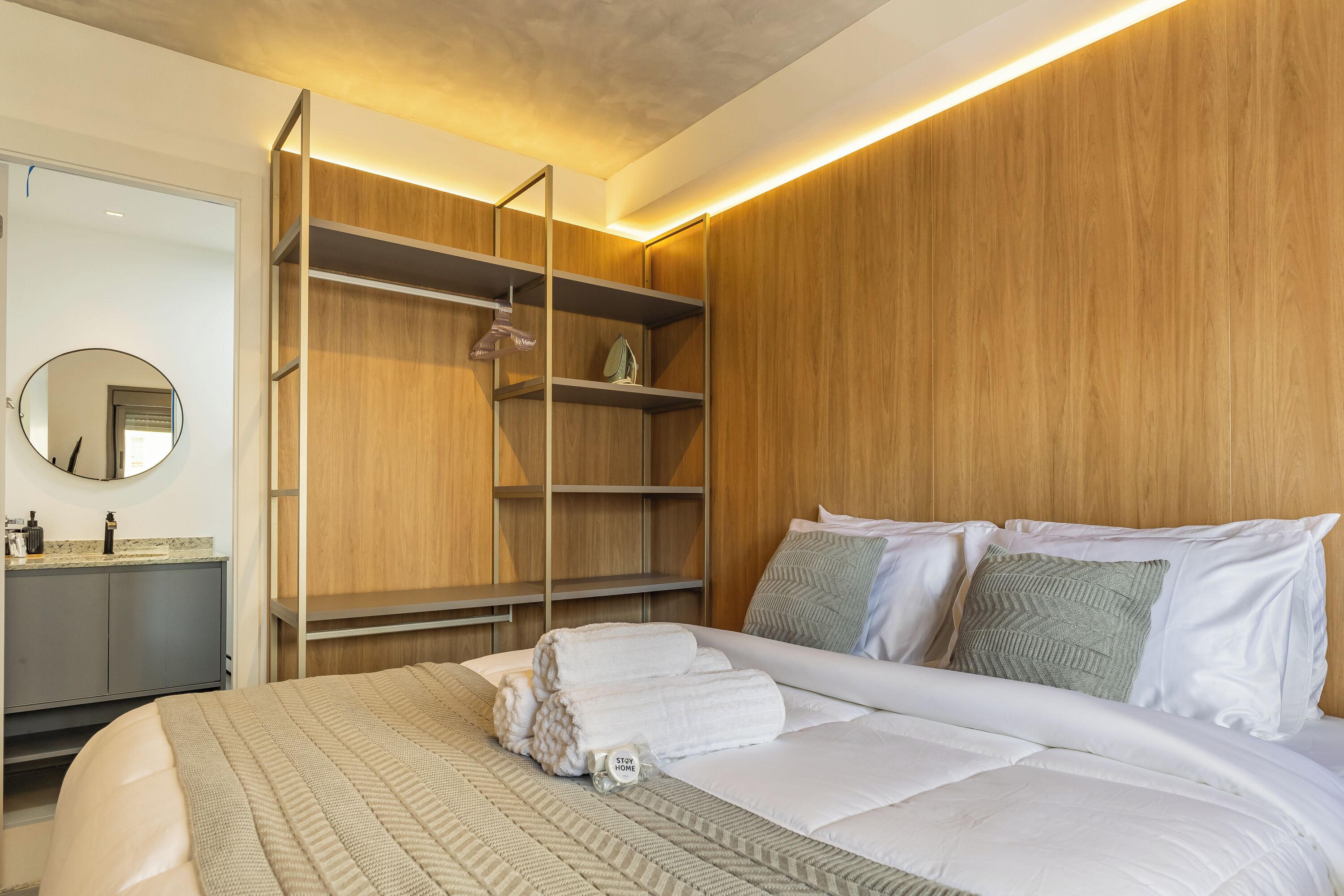 Quarto de hotel com cama, guarda-roupa de madeira, espelho e banheiro com pia e espelho.