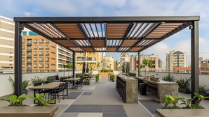 A rooftop terrace with outdoor seating, potted plants, and a view of surrounding buildings. - Stay Home João Cachoeira - Piscina - Gym (São Paulo)