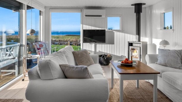 Een moderne woonkamer met een witte bank, een salontafel en een televisie. Er is een groot raam met uitzicht op zee en een balkon.