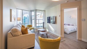 A modern living room with a sofa, chairs, a TV, and a bed in the adjacent room. - ⚽ FIFA World Cup 2026 | Furnished Coal Harbour Condo | Parking Included (Vancouver)