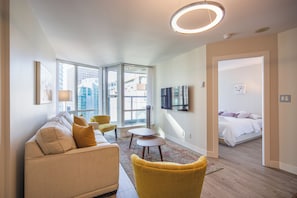A modern living room with a sofa, chairs, a TV, and a bed in the adjacent room.