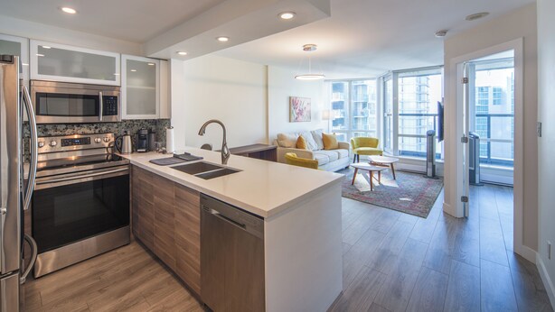 A modern kitchen with stainless steel appliances, a central island, and a dining area with a yellow chair. - ⚽ FIFA World Cup 2026 | Furnished Coal Harbour Condo | Parking Included (Vancouver)