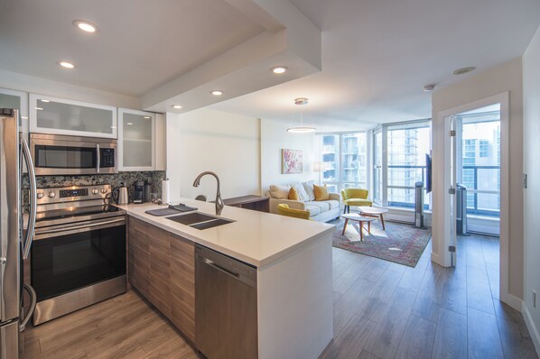 A modern kitchen with stainless steel appliances, a central island, and a dining area with a yellow chair.