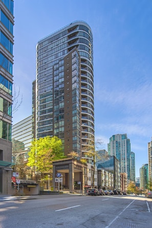 A tall, curved building with multiple floors and balconies, surrounded by other high-rise buildings.