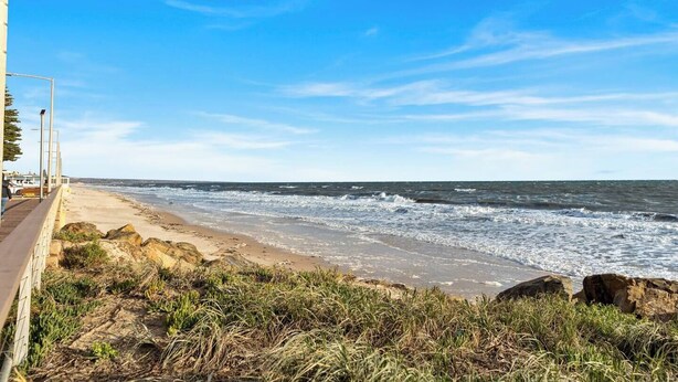 Een kustgezicht met een zandstrand, rotsachtige rotsformaties en een helderblauwe lucht.