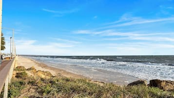 A coastal view with a sandy beach, rocky outcrops, and a clear blue sky.