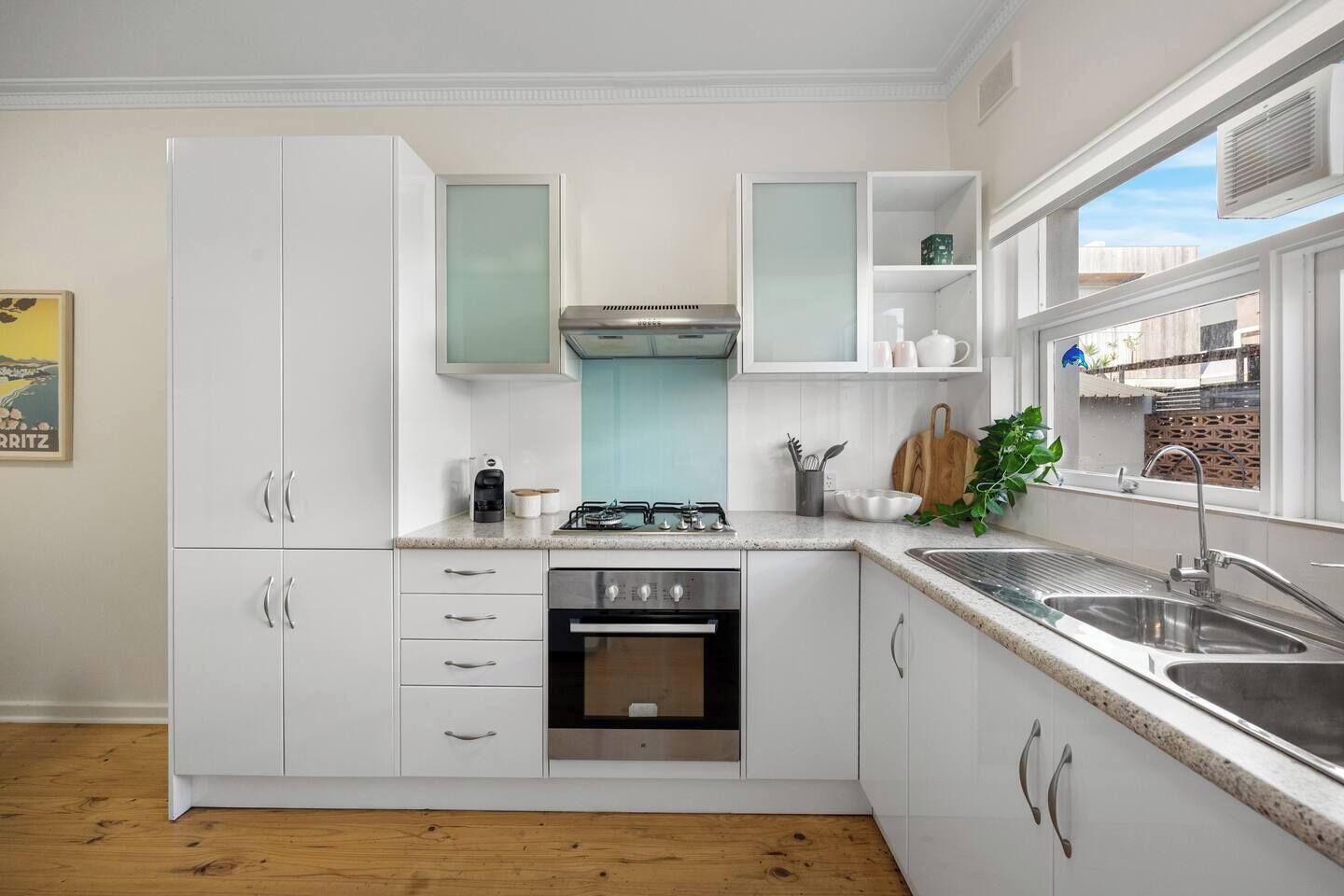 A modern kitchen with white cabinets, a gas stove, an oven, a sink, and a window with a view of buildings.