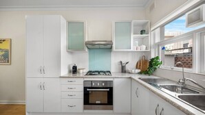 Een moderne keuken met witte kasten, een gasfornuis, een oven, een spoelbak en een raam met uitzicht op gebouwen.