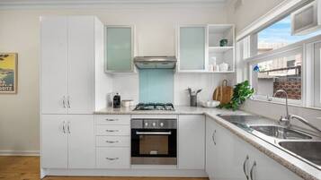A modern kitchen with white cabinets, a gas stove, an oven, a sink, and a window with a view of buildings.
