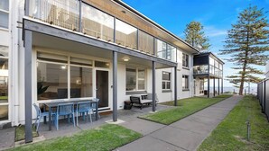 Een modern gebouw met twee verdiepingen, een overdekt terras, een eethoek met blauwe stoelen en uitzicht op zee.