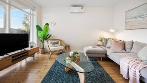 Een woonkamer met een televisie, een bank, een stoel, een salontafel en een grote plant.