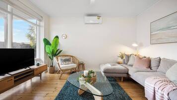A living room with a TV, a sofa, a chair, a coffee table, and a large plant.