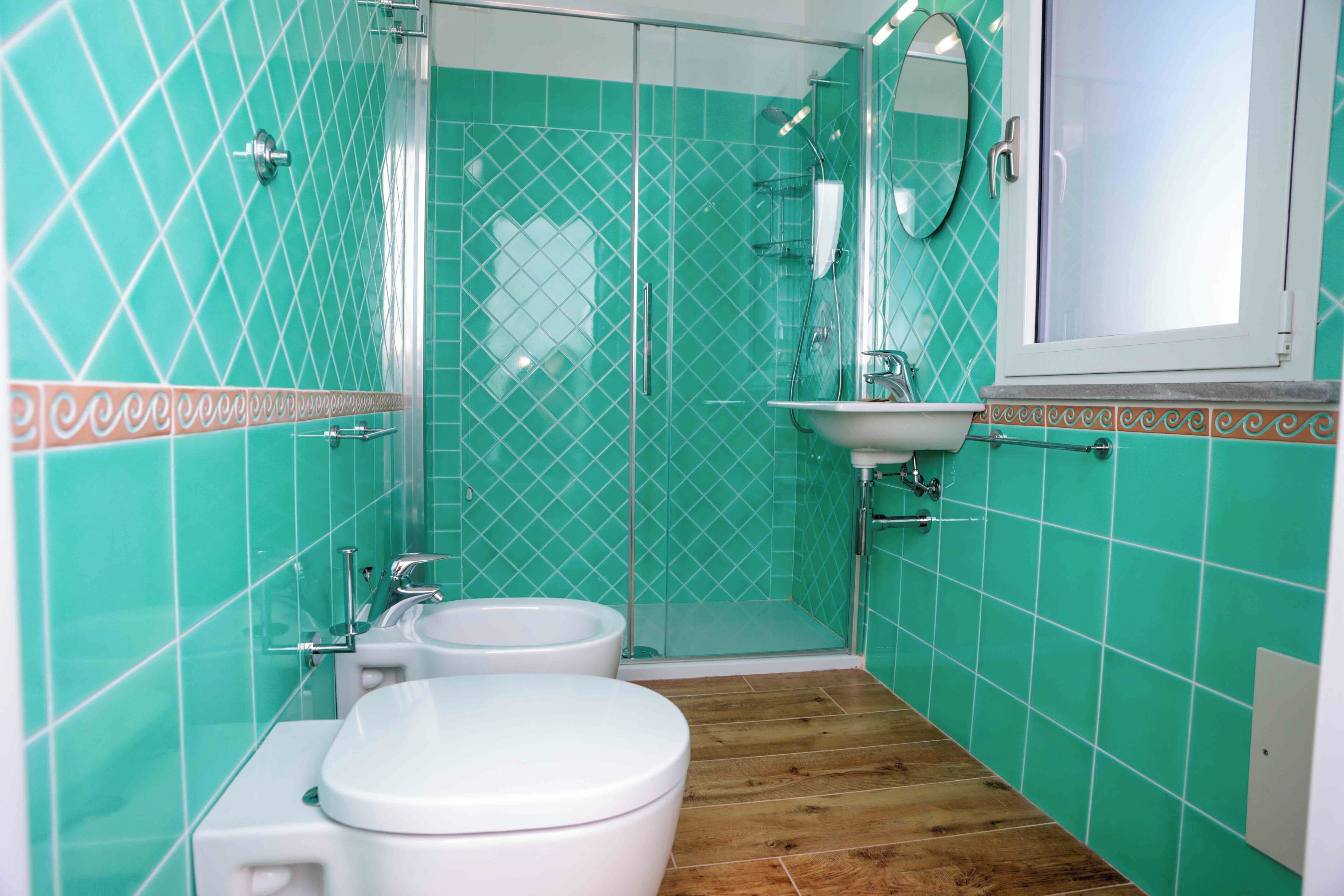 Un bagno con doccia, WC e lavandino, il tutto con piastrelle verdi.