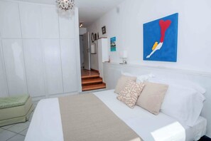 A bedroom with a bed, pillows, a wall-mounted painting, and a staircase leading to another room.