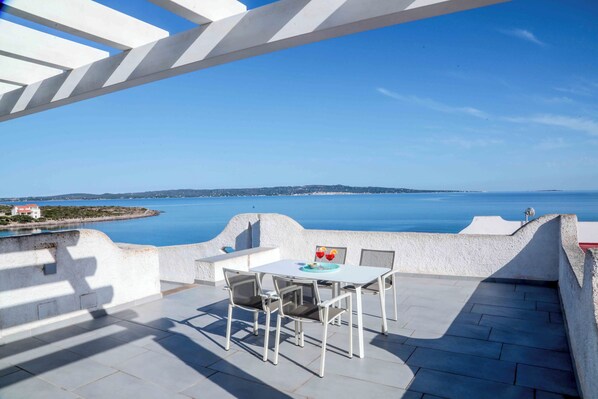 A terrace with a table and chairs, overlooking a body of water and a distant coastline.