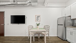 Een moderne keuken met witte kasten, een roestvrijstalen koelkast en een flatscreen televisie aan de muur.