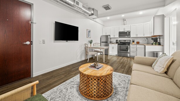 Een moderne woonkamer met een bank, een ronde houten salontafel, een televisie en een keuken op de achtergrond.