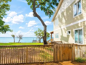 Ein Haus mit einer Holzterrasse, Blick auf das Wasser und einem Rasen.