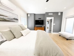 Ein modernes Schlafzimmer mit einem großen Bett, einem Flachbildfernseher, einem Schminktisch und einem begehbaren Kleiderschrank.