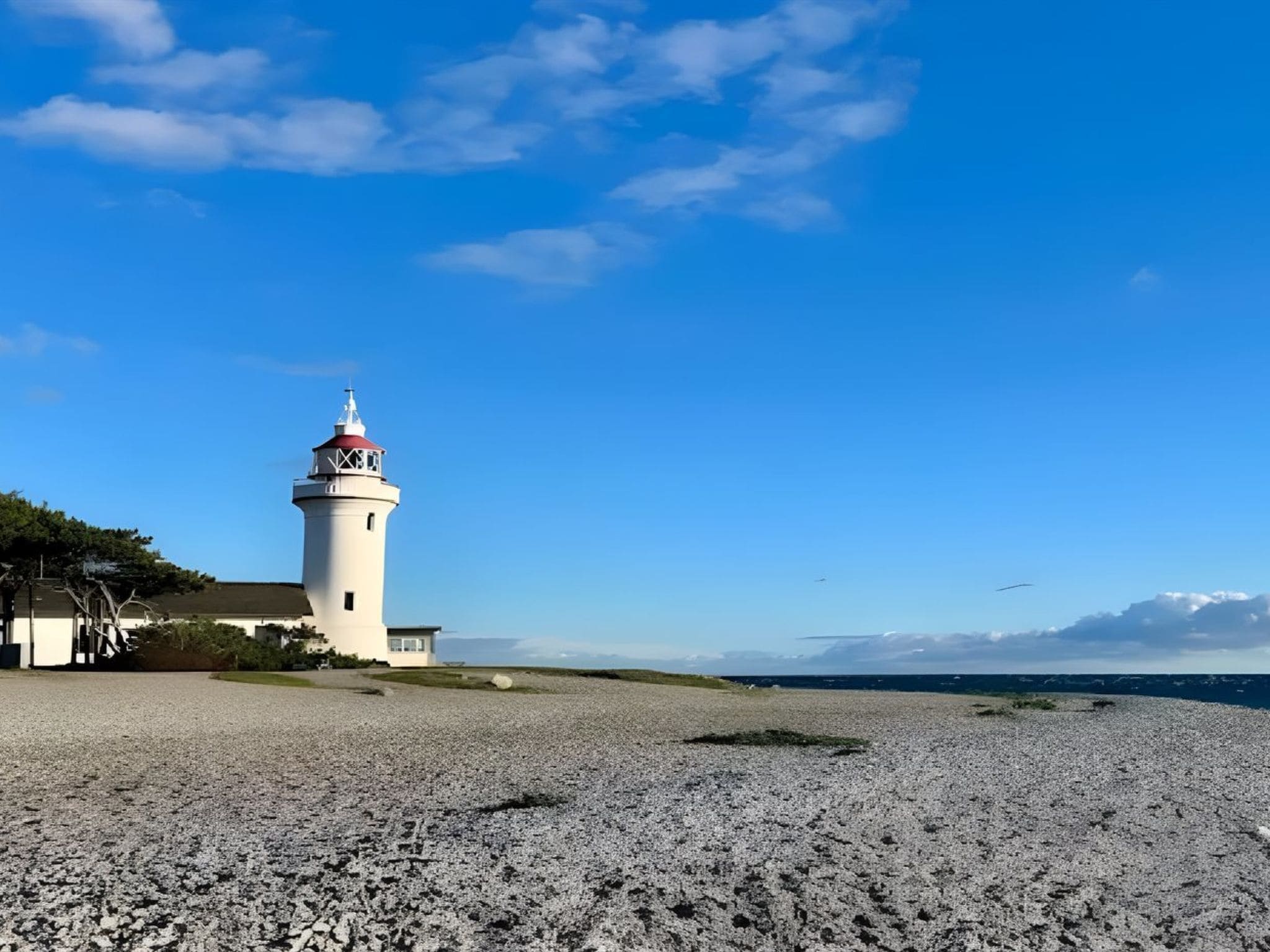 A lighthouse on a pebbly beach with a clear sky.