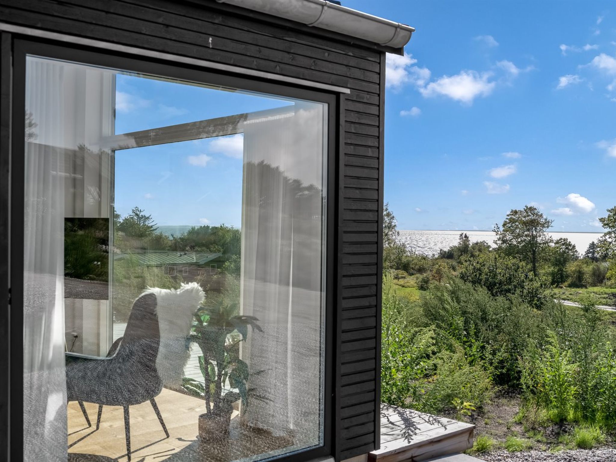 A modern room with a large sliding glass door leading to an outdoor area with a view of a body of water and greenery.