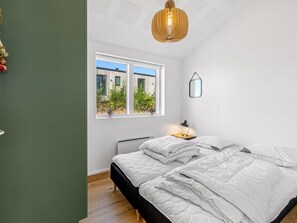 Ein Schlafzimmer mit Bett, Nachttisch mit Lampe, Fenster mit Blick auf Grünflächen und einer Hängeleuchte.