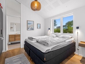 Une chambre à coucher moderne, avec un lit, une lampe de chevet, une fenêtre et une porte donnant sur une salle de bain.