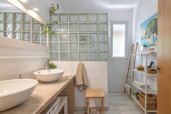 A bathroom with two sinks, a mirror, a towel rack, a wooden stool, a ladder, and a shelf with baskets.