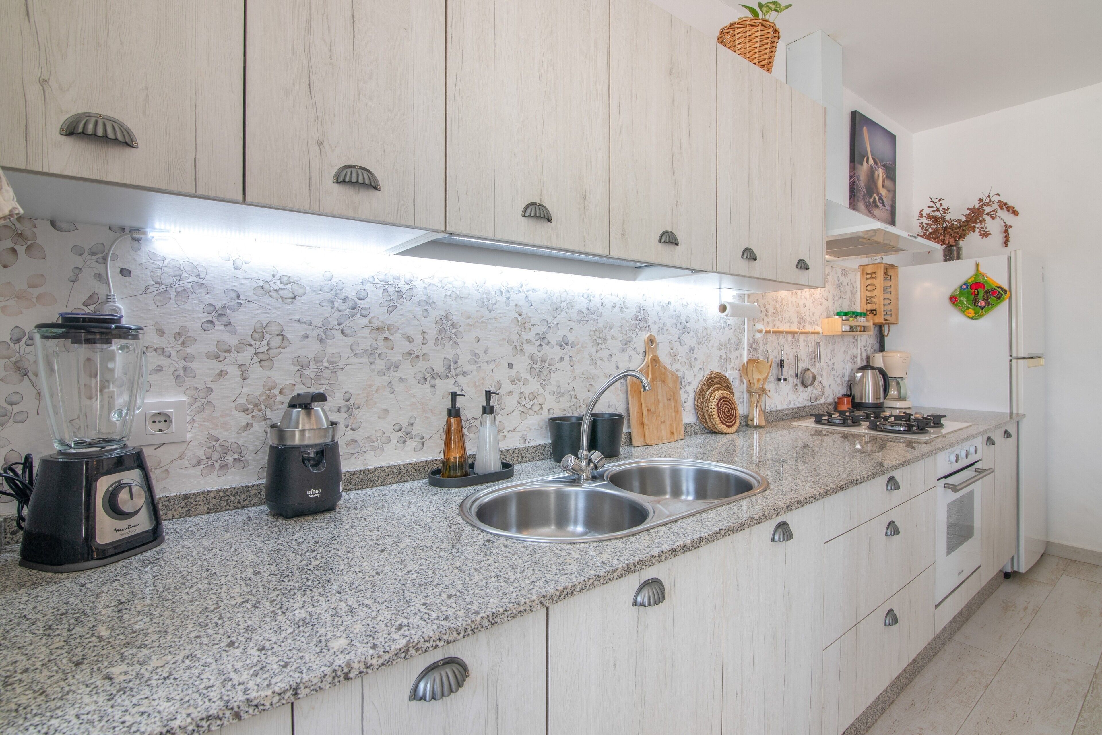 A kitchen with a granite countertop, stainless steel sink, and white cabinetry.