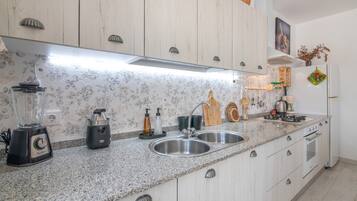 A kitchen with a granite countertop, stainless steel sink, and white cabinetry.
