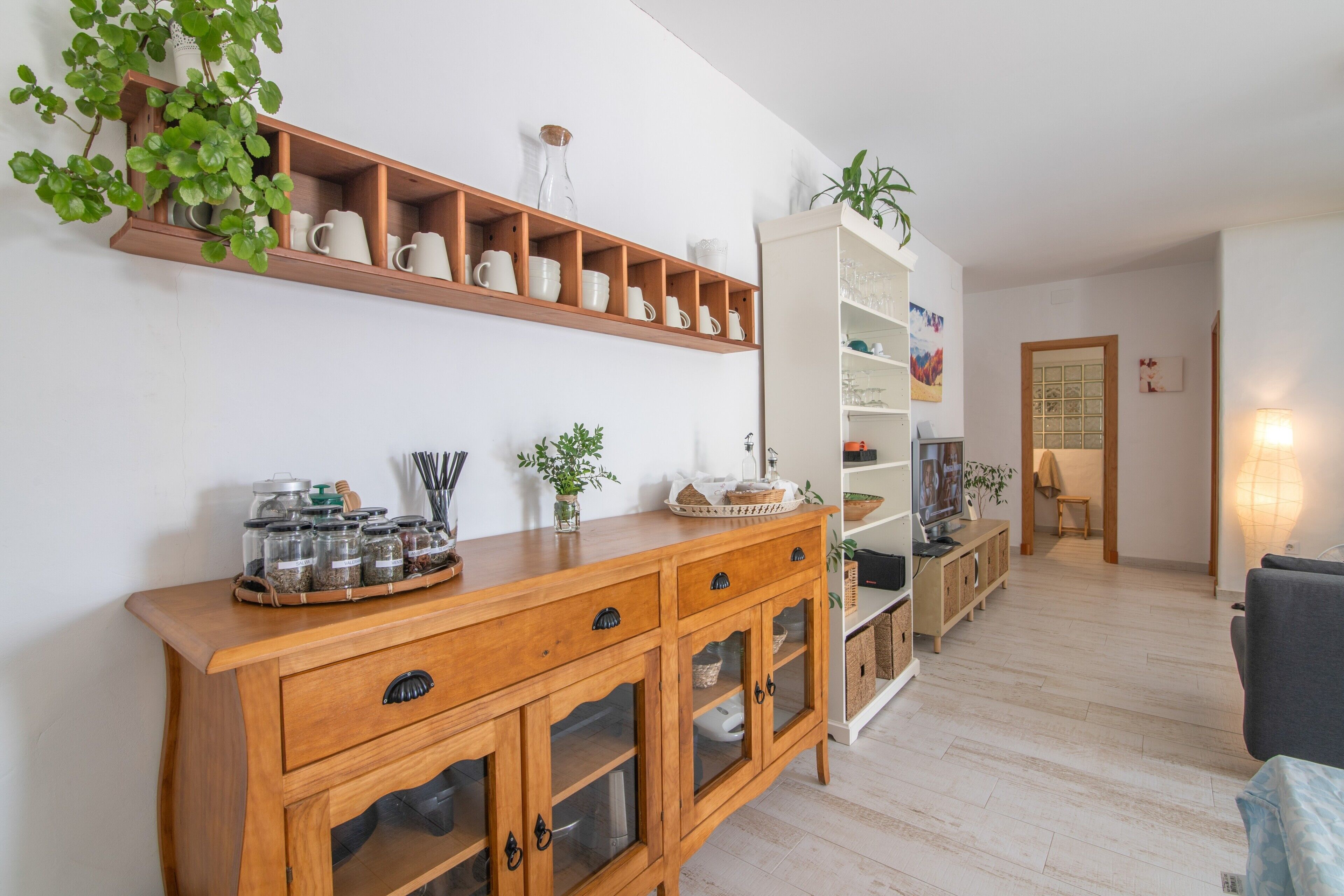A wooden cabinet with drawers and glass doors, a shelf with white mugs, and a potted plant.