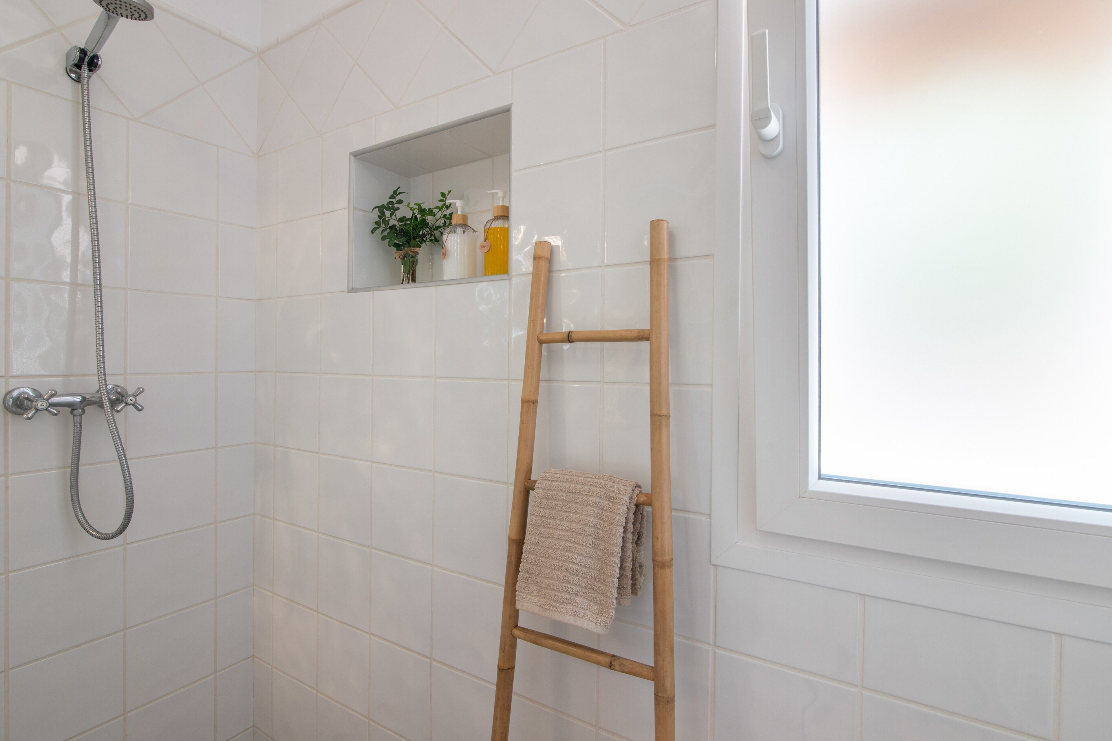 Een douche met een handdouche, een houten ladder en een plank met toiletartikelen.